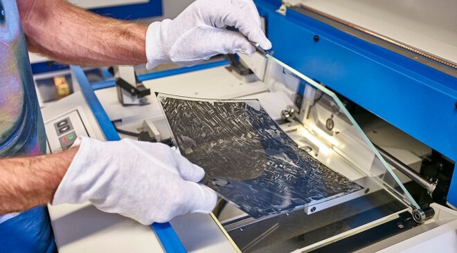 ein Luftbildnegativ wird zwischen Glasplatten auf den Scanner gelegt; der Mitarbeiter trägt weiße Stoffhandschuhe